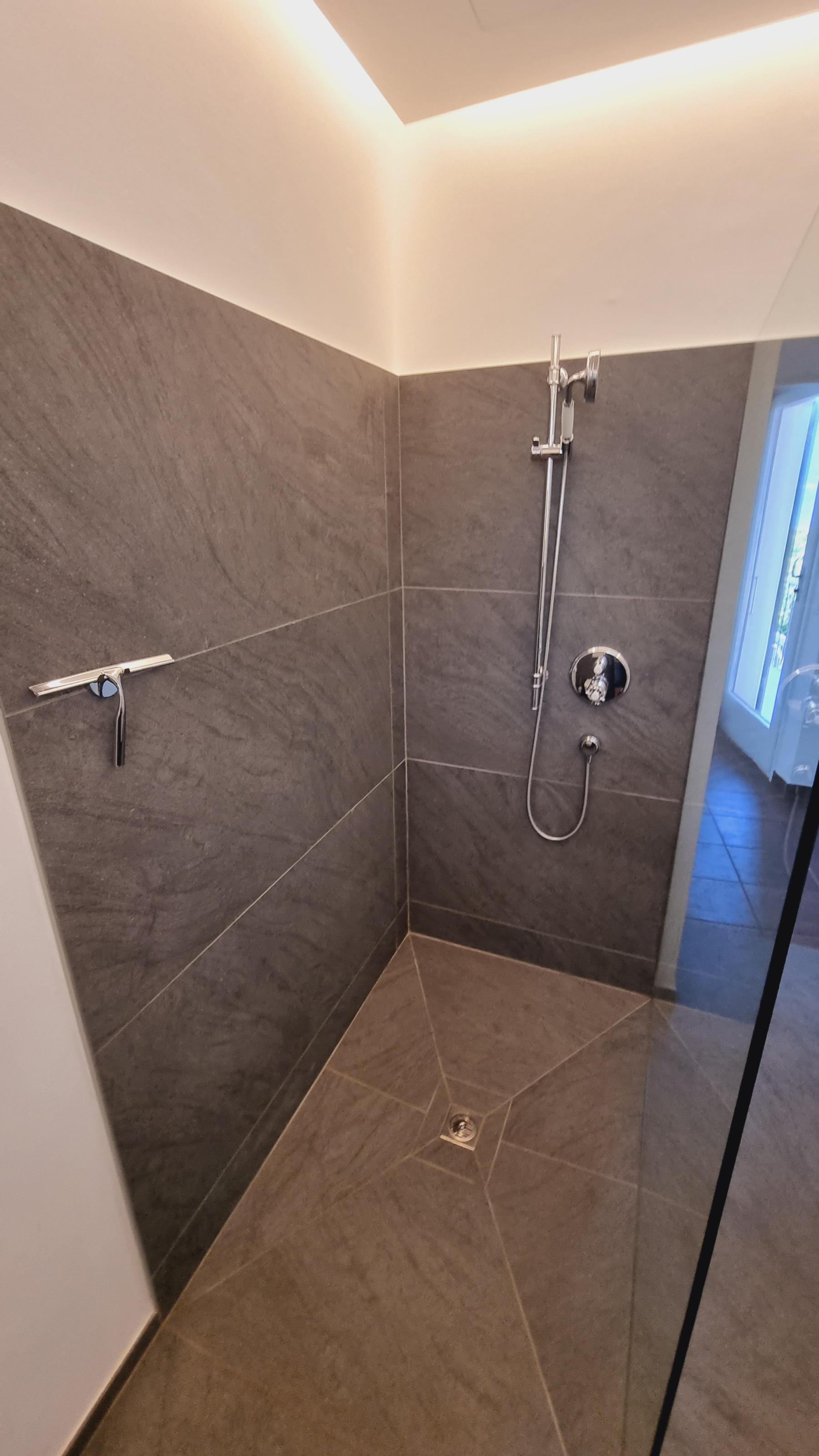 Eine grosszügige, offene Dusche verleiht Ihrem Badezimmer einen charmanten und natürlichen Stil. Das Bild zeigt die ganze Dusche mit Glasduschwand